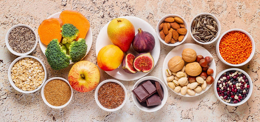 Eine Auswahl gesunder Lebensmittel, darunter Obst (Äpfel, Feigen), Gemüse (Brokkoli, Kürbis), Hülsenfrüchte (Linsen, Bohnen), Nüsse, Samen (Chia, Sonnenblumenkerne), Vollkornprodukte und dunkle Schokolade.